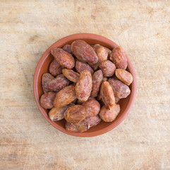 Honey glazed almonds in a small bowl on an old wood cutting board.