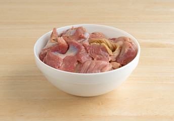 Bowl of fresh chicken gizzards and hearts atop a wood table.