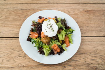 Delicious salad with salmon, baked potatoes, lettuce and mushrooms served on a white plate on old wooden table