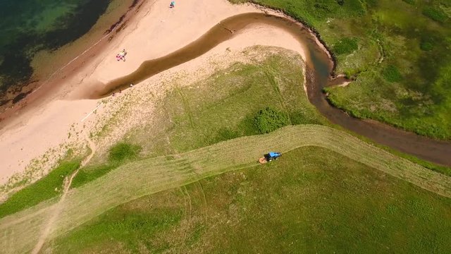 Aerial high shot a farmer cutting grass on a field by ocean cove
