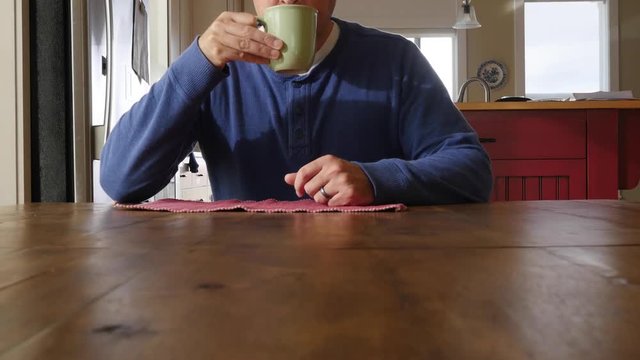 A man sits down at a wooden table in morning for coffee