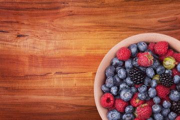 Brown ceramic plate with berries on the right bottom corner of the wooden table with clipping path. Top view.