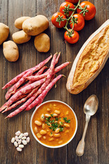Bean soup in white bowl surrounded by ingredients on wooden table