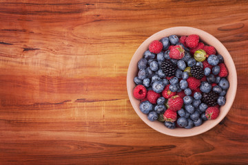 Brown ceramic plate with berries on the right of the wooden table with clipping path. Top view.