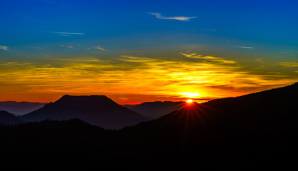 Fototapeta na wymiar Idyllic sunset landscape with silhouettes of mountains and vivid