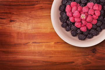 Ceramic plate with heart shaped berries on the right top corner of the wooden table with clipping path. Top view.