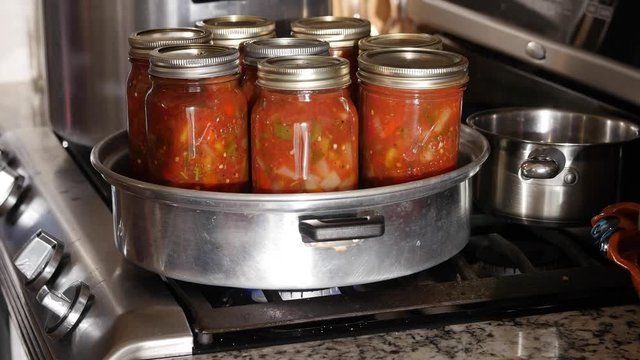 A woman preserving homemade peach salsa in kitchen