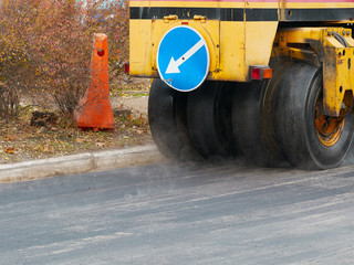 Road construction works with tyred road roller finishes asphalt