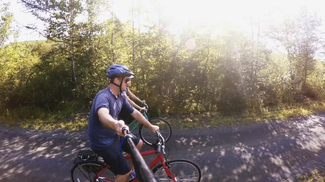 A fun shot of a couple biking in a green forest on bike trail