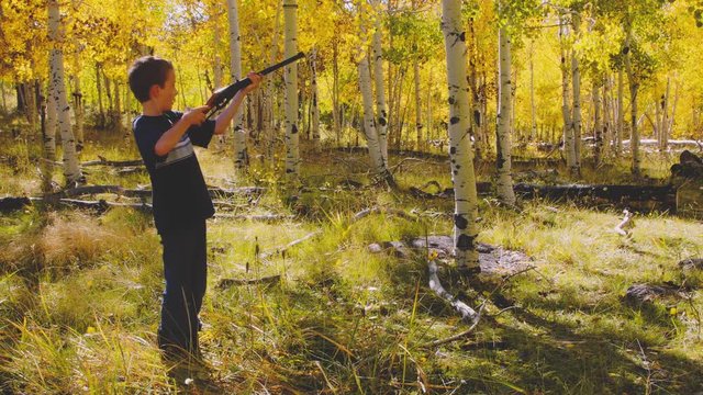 A boy shoots a bb gun while camping in the woods