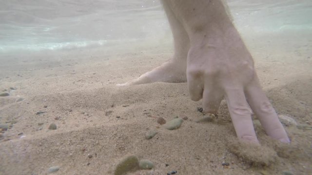 Hand picks up rocks on ocean floor to skip on surface
