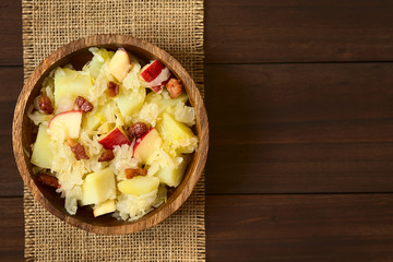 Salat aus Sauerkraut, Apfel, Kartoffeln und Speck in Holzschüssel, fotografiert mit natürlichem Licht (Selektiver Fokus, Fokus auf den Salat)