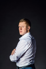 Serious man standing sides in a half-turn with folded hands. Studio shot.