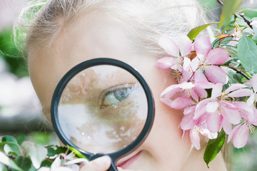 Girl child with a magnifying glass in flowers, spring.