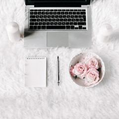 Square crop. Freelance woman workspace in flat lay style with laptop, vintage tray, roses, notebook and pen on white fur background. Top view, flat lay. Freelance concept.