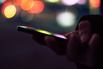 Smart phone in male hands in front of blurred city lights