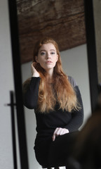 Fototapeta na wymiar Red Haired Woman in Black Dress Looking at Herself in a Mirror