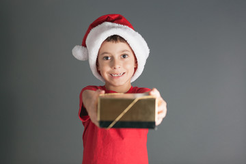 Smiling funny child in Santa red hat holding Christmas gift in hand. Christmas concept