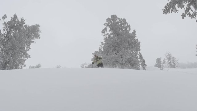 A man makes a deep turn past camera, blowing snow onto the lens
