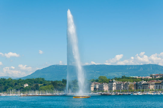 Geneva skyline with famous Jet d'Eau fountain and traditional boat at harbor district in Canton of Geneva, Switzerland