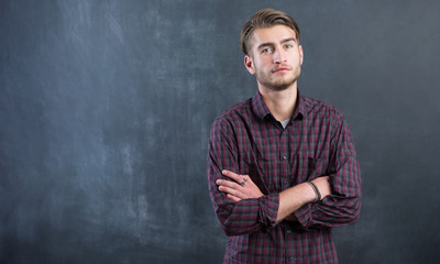 Happy young man standing with arms crossed over blackboard backg