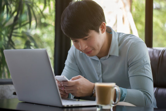 Young Asian Man Using Laptop And Smart Phone In Cafe