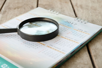 Blurred calendar page with Magnifying Glass on wood background.