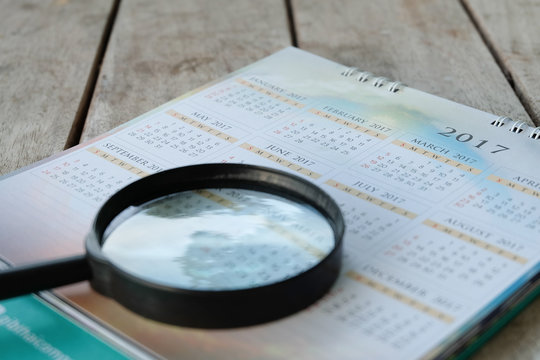 Blurred calendar page with Magnifying Glass on wood background.