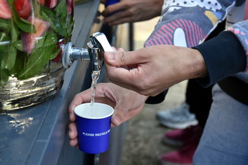 Man's hand unscrews the faucet which drops the fresh water into a glass. Filling A Glass Of Water From Tap. Jugs full of with water and fruits, orange, strawberry, lemon.
