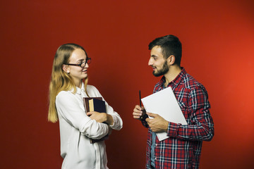 Two teenager students have a friendly study discussion holding books on red background