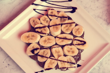 Dessert with banana and chocolate on a white square plate. Toned
