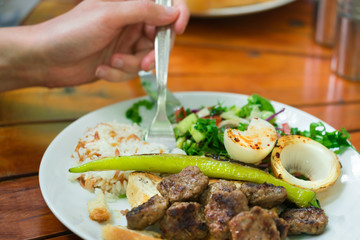 Hand with a fork and roast meat with salad in a white plate on a wooden table