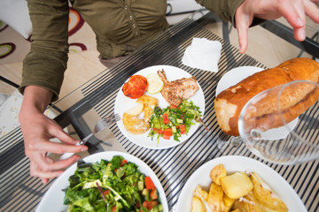 Woman with a fork sitting at the table with salad, bread, chicken, potatoes on white plates