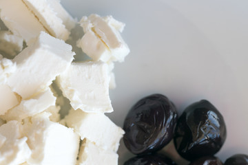 Black sun-dried olives and feta cheese slices on a white background