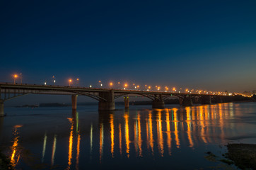 Fototapeta na wymiar Bridge with bright lights across the river at night and reflecti