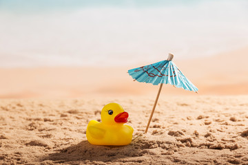 Umbrella and rubber duck in sand against backdrop of coast.