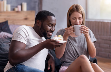 Overjoyed couple drinking tea with cupcakes in bedroom