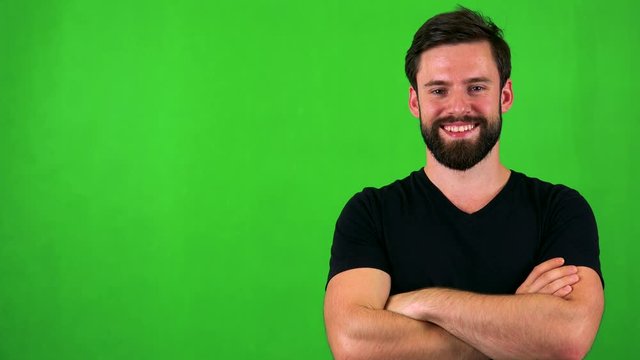 young handsome bearded man smiles to camera with folded arms - green screen 
