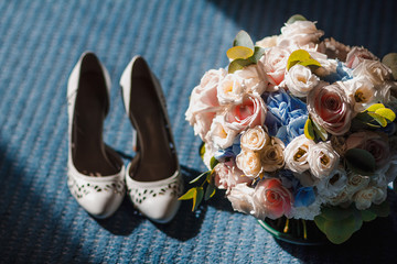 Wedding accessories shoes and bride's bouquet illuminated by dramatic light