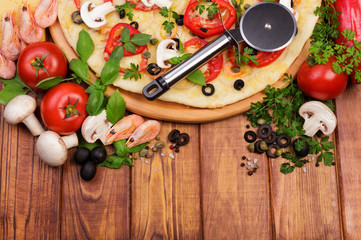 Pizza with shrimp, mushrooms, vegetables, knife wheel on dark wood.