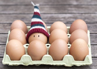 Egg wearing a knitted hat souronded by brown eggs.
