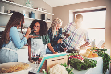 Friends tasting food at table in kitchen