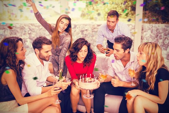 Composite image of woman blowing birthday candles with friends