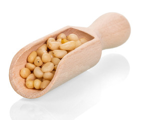 Pine nuts in wooden scoop, close-up isolated on white.