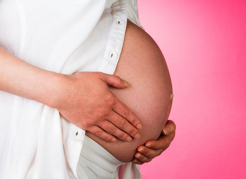 Pregnant woman supports hands stomach on pink background.
