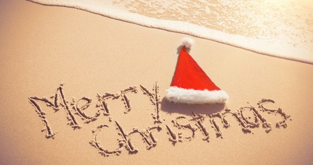 Merry Christmas written on sand with santa hat