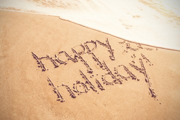 Happy holiday written text on sand