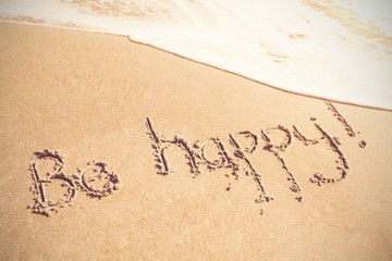 Fototapeta na wymiar Be happy text written on sand