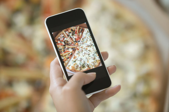 Female hand making a photo of pizza, with a mobile phone, close up, horizontal