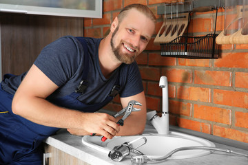 Handsome plumber replacing faucet in kitchen, close up view